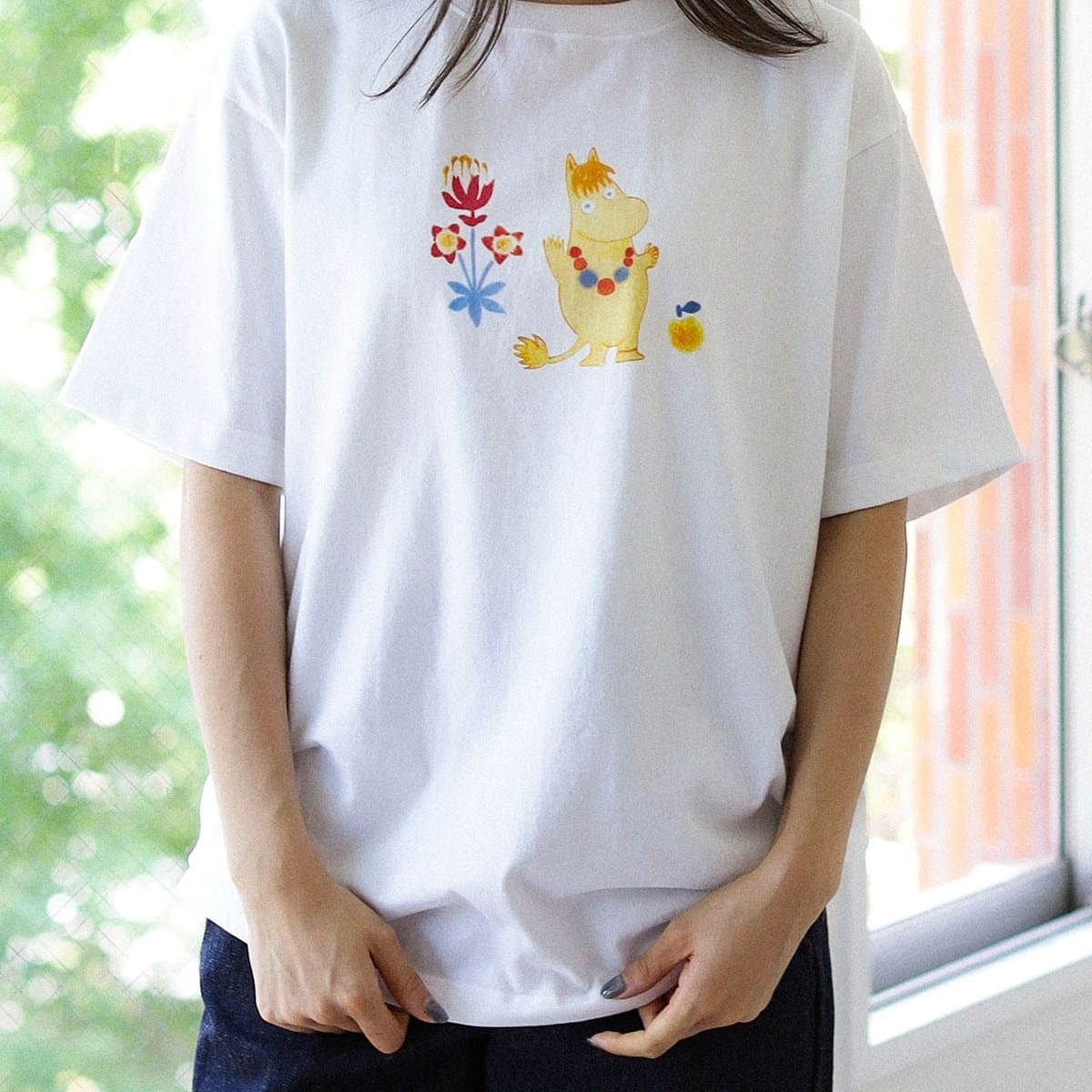 Mumin T-shirt Snorkfröken M Beams - White t-shirt with a colorful Snorkmaiden design worn by a person, with a blurred background.
