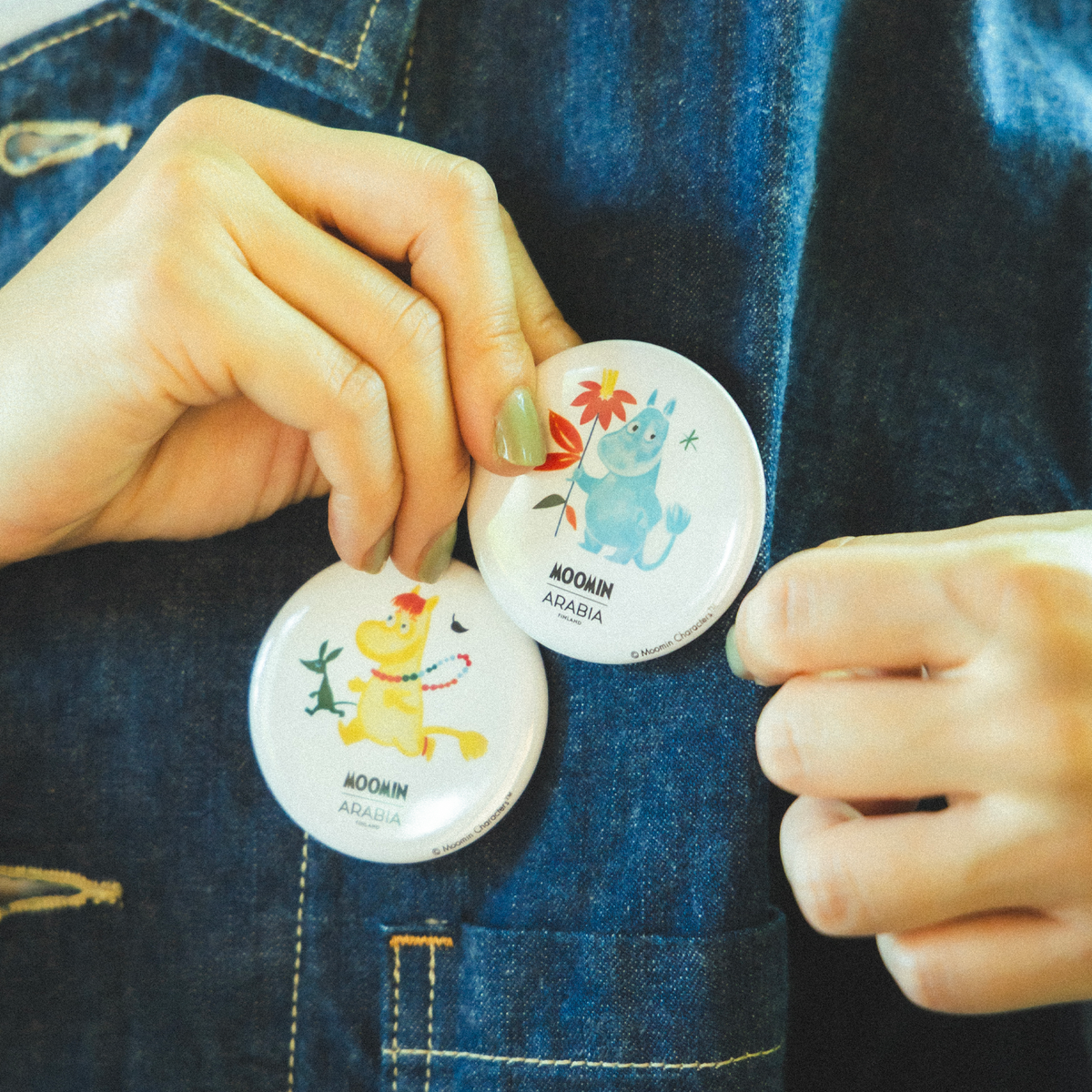 Moomin badge set, Beams -  A person wearing a denim jacket putting on a Snorkmaiden and Moomintroll badges.