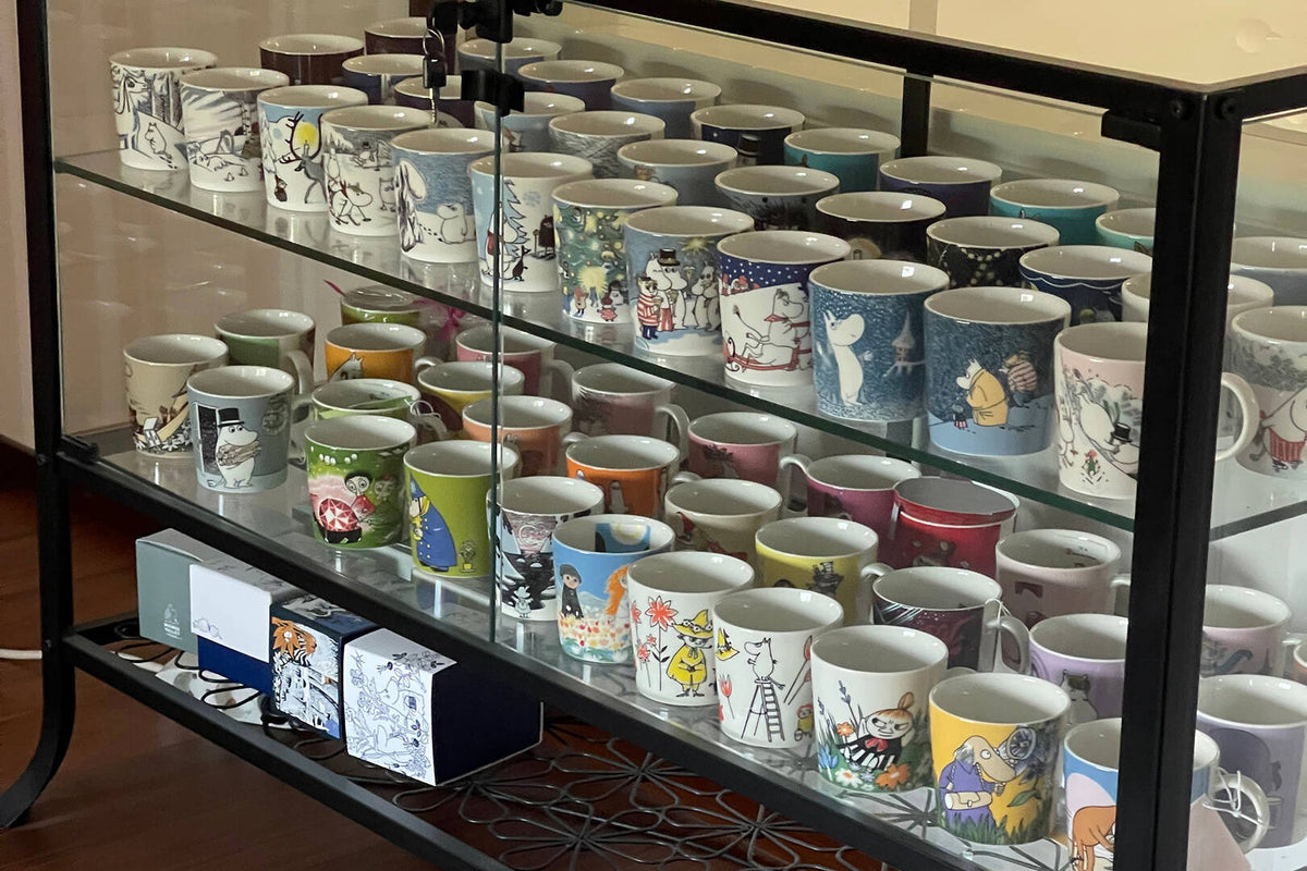 Display case filled with variously designed ceramic Moomin mugs.