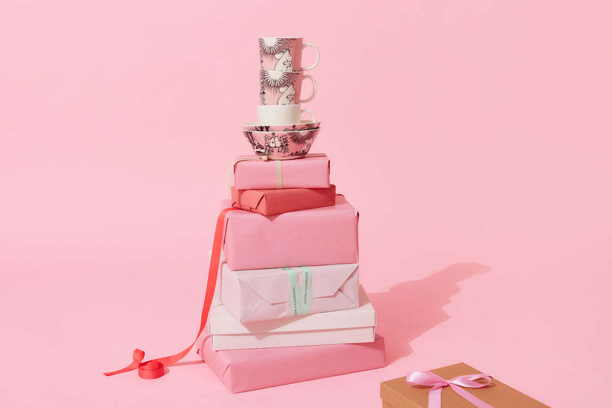 Stack of pink gift boxes with Moomin Love mugs and bowls on top on a pink background