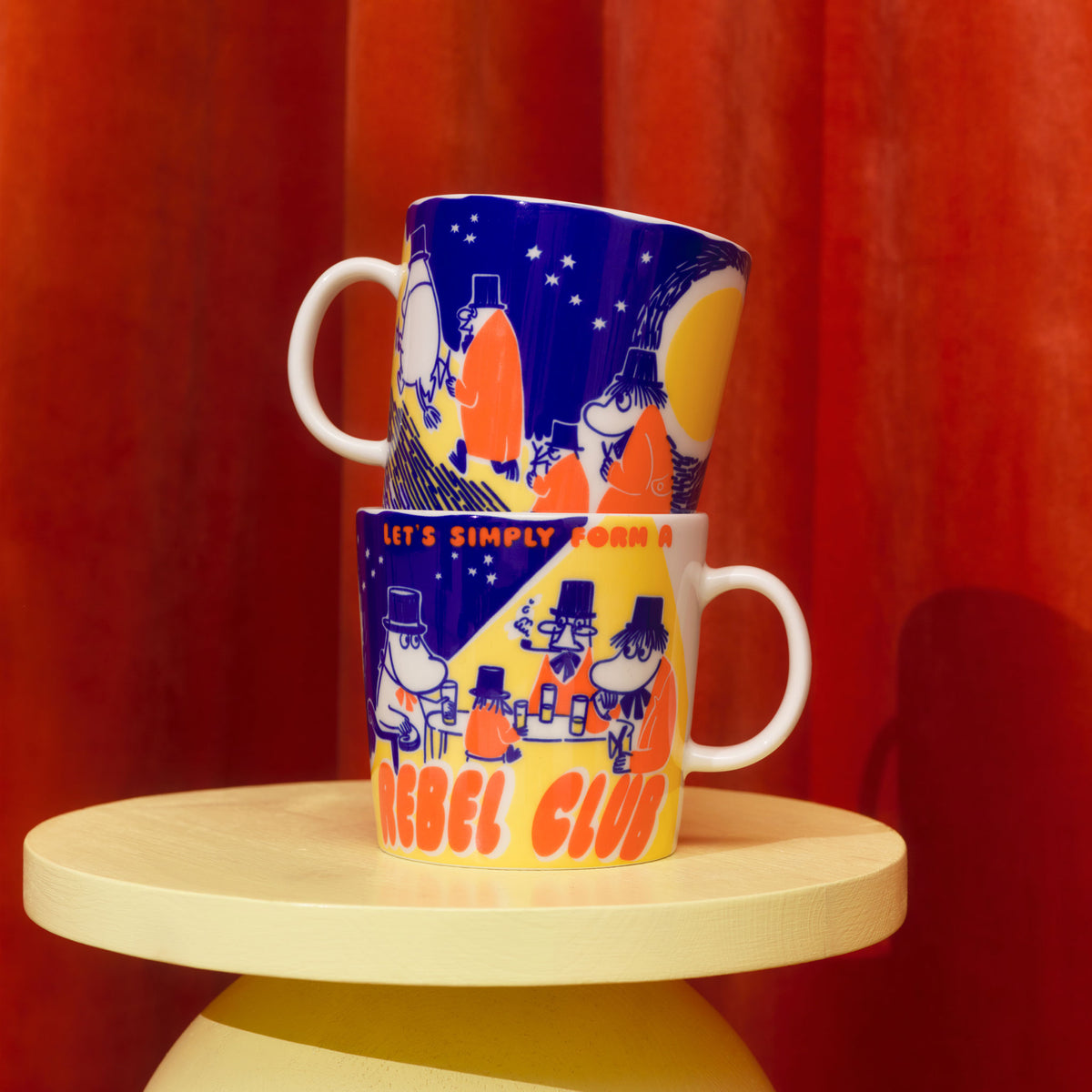Mummi kopp 0,4 l Rebel Club - TwoRebel Club mugs stacked on a wooden stool against a red curtain background