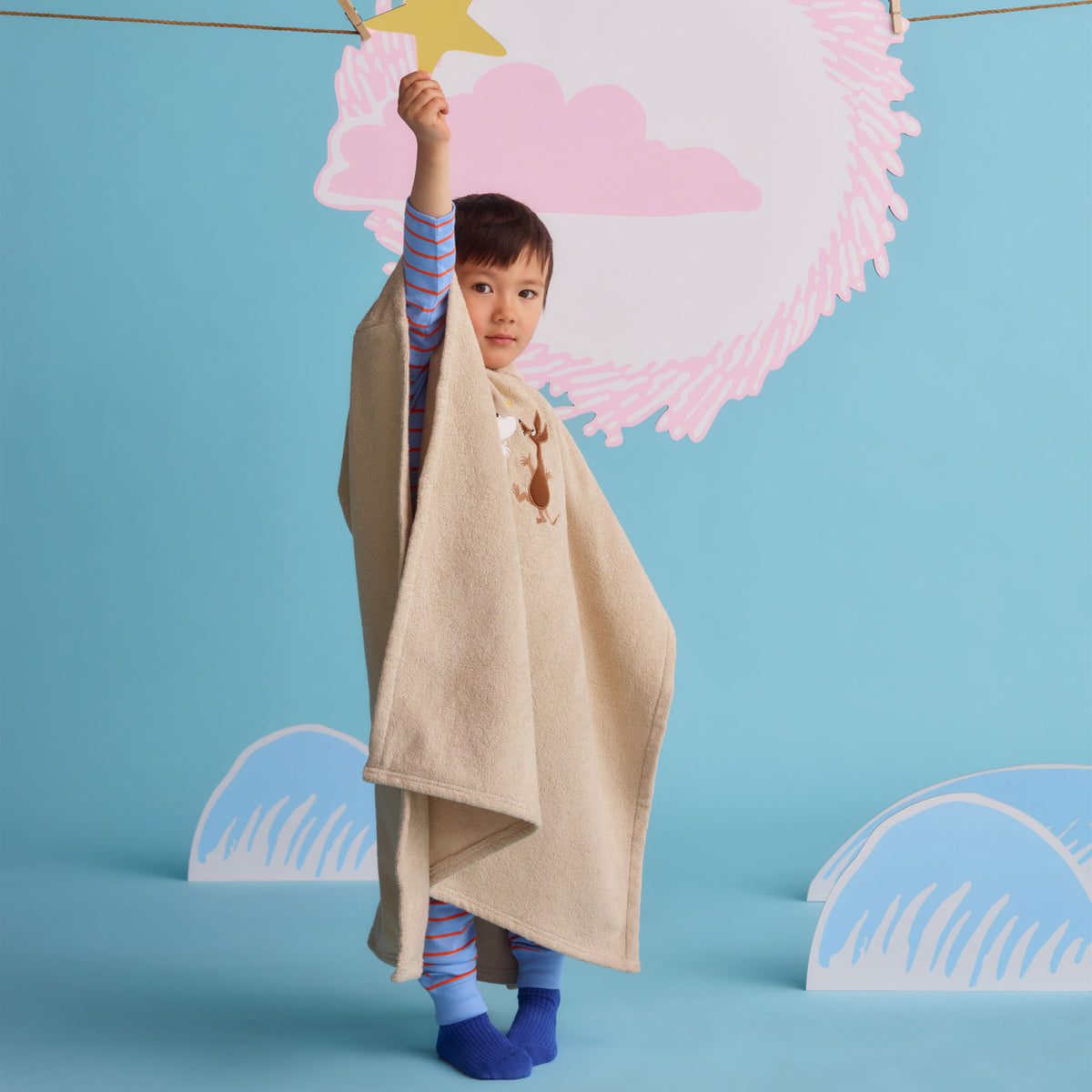 Moomin kids bath poncho Space Adventure - A child wearing a beige poncho towel holding up a star cut out.