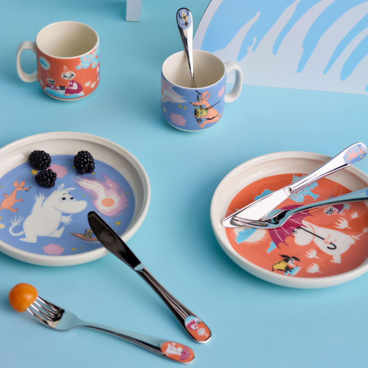 Mummi barnesett Under paraplyen - A styled flat-lay of a Space Adventure themed ceramic tableware set on a light blue background, including plates, mugs, cutlery, and utensils.