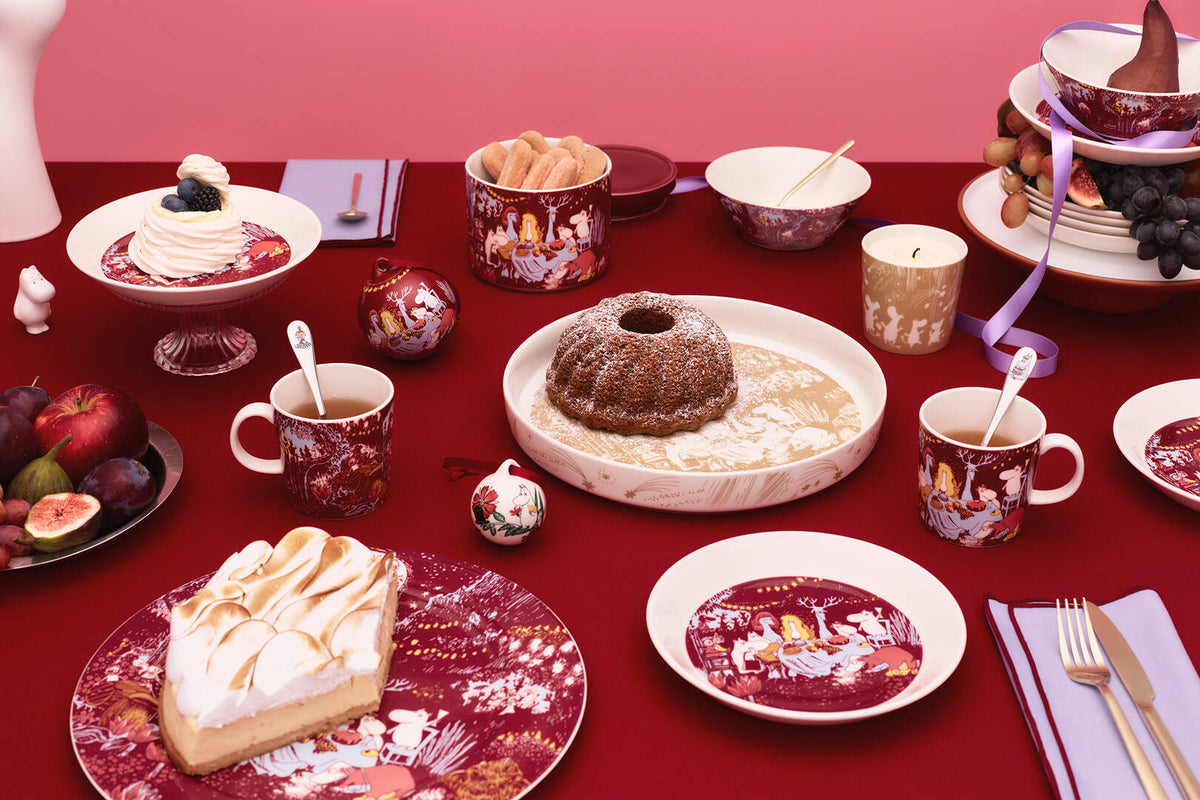 Christmas table setting with various desserts and Moomin festive moments -mugs on a red tablecloth