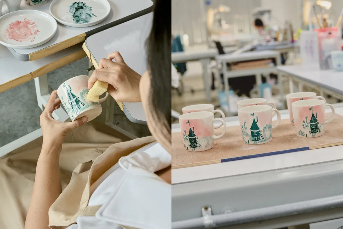 Person giving finishing touches to a home-mug with a scenic design. 