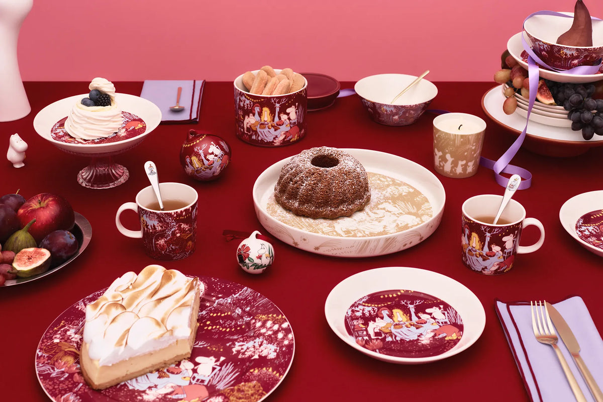 Festive table setting with various desserts and Moomin Arabia Festive moments -mugs, plates and bowls on a red tablecloth