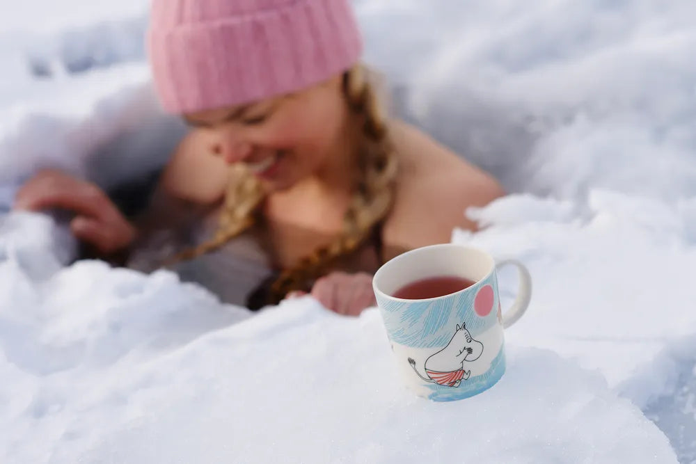 Person in pink beanie ice swimming with a mug featuring a moomintroll.