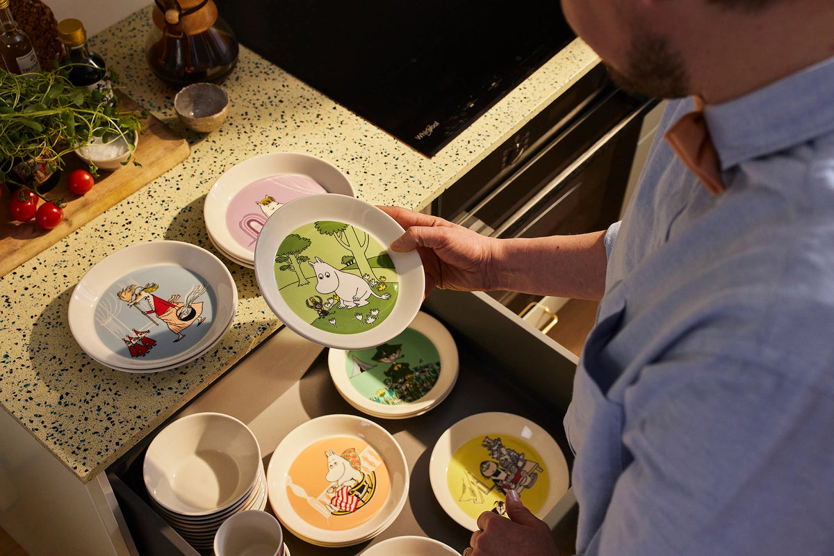 Person holding a plate with Moomin character design in a kitchen setting