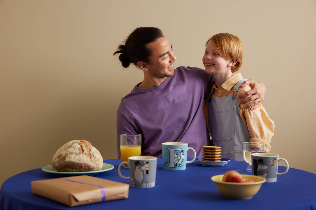 Father and son sitting at a table with food and drinks, smiling and embracing.
