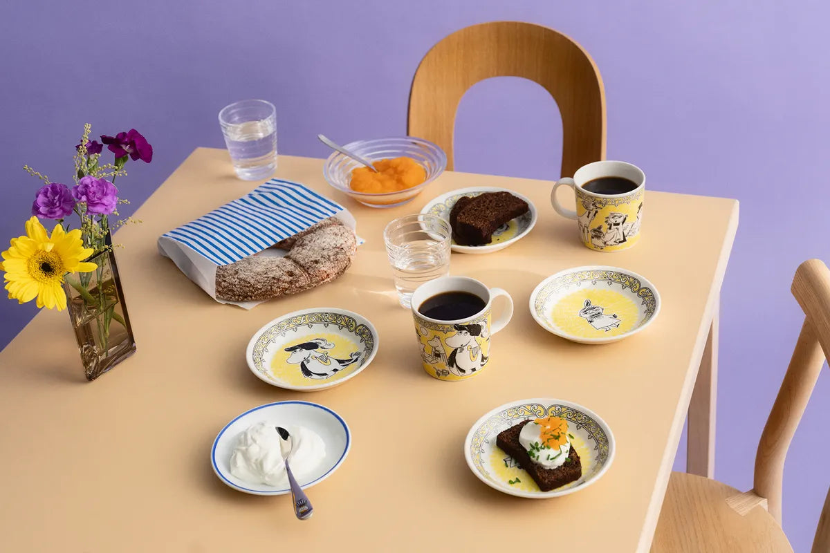 Table setting with Moomin opera collection for scope -plates, cups, and food on a purple background